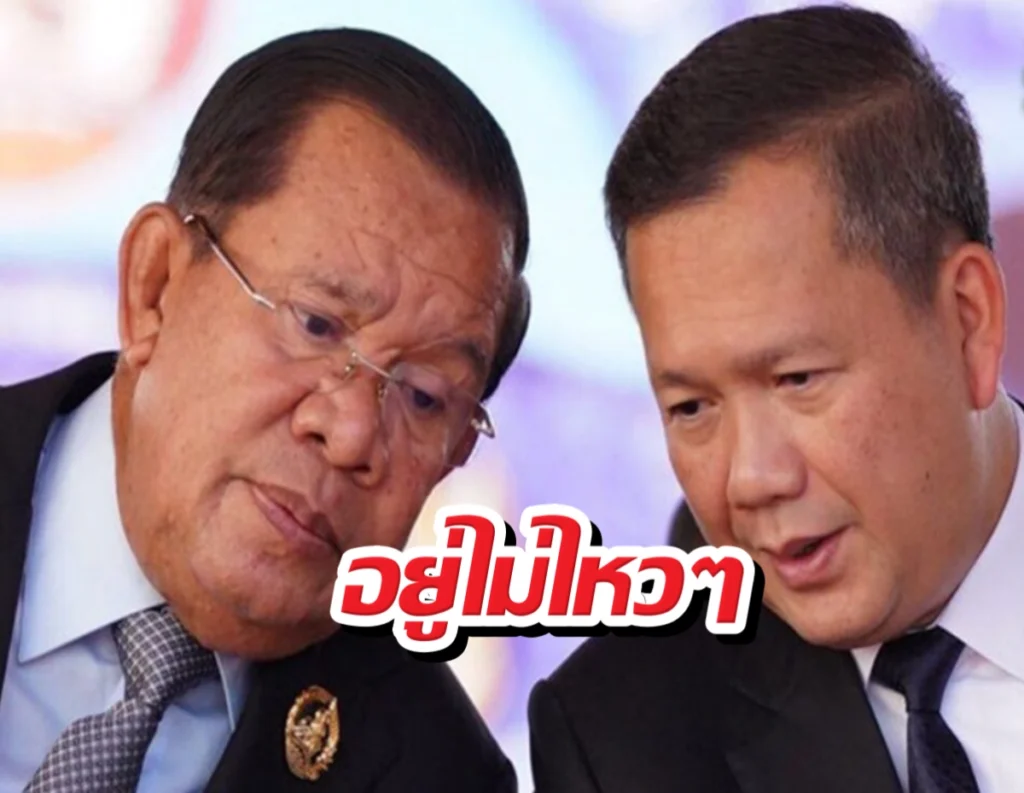 Two men in suits lean in and talk closely on stage, with bold red Thai text overlaid.