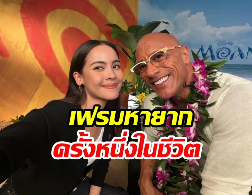 Smiling young woman and a bald man with glasses wearing a flower lei pose for a selfie in a tropical backdrop resembling Moana.