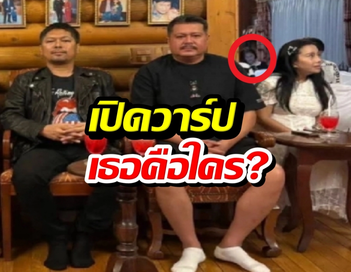 Three adults sit on a wooden sofa in a cozy log-cabin room; a small figure is circled in red in the background behind the center man.