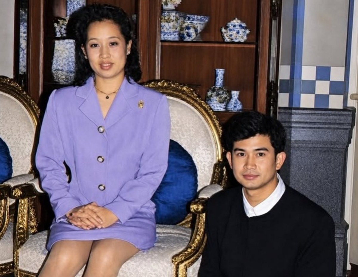 Woman in a lavender blazer sits on a gold-trimmed chair, hands folded, with a man in a dark sweater beside her in a room filled with blue-and-white porcelain.