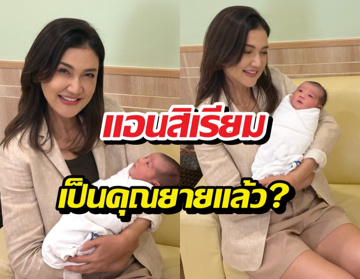Smiling woman in a beige blazer sits on a yellow couch, cradling a swaddled newborn; Thai text overlay asks if she’s now a grandmother.